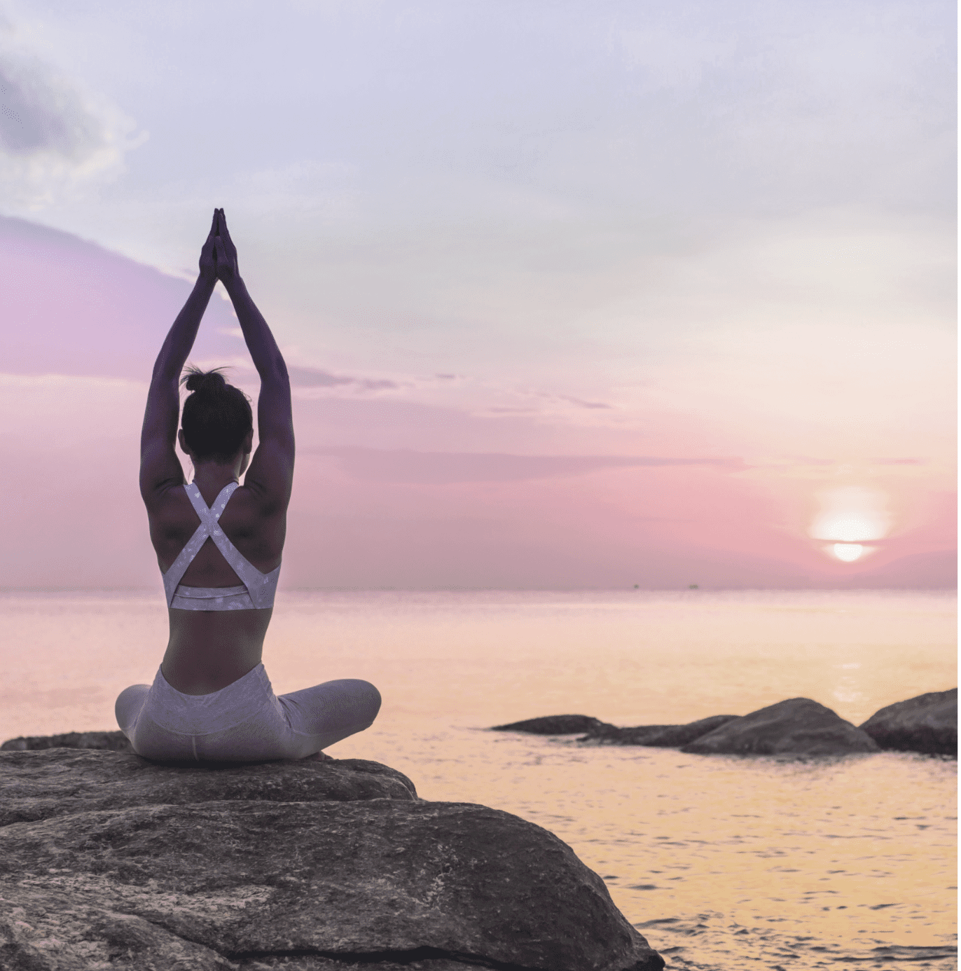 Yogadame auf einem Stein vor einem Sonnenuntergang am Strand