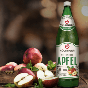 Höllinger steirischer Apfelsaft in der Mehrweg-Flasche auf einem Holz Tisch mit Äpfeln.