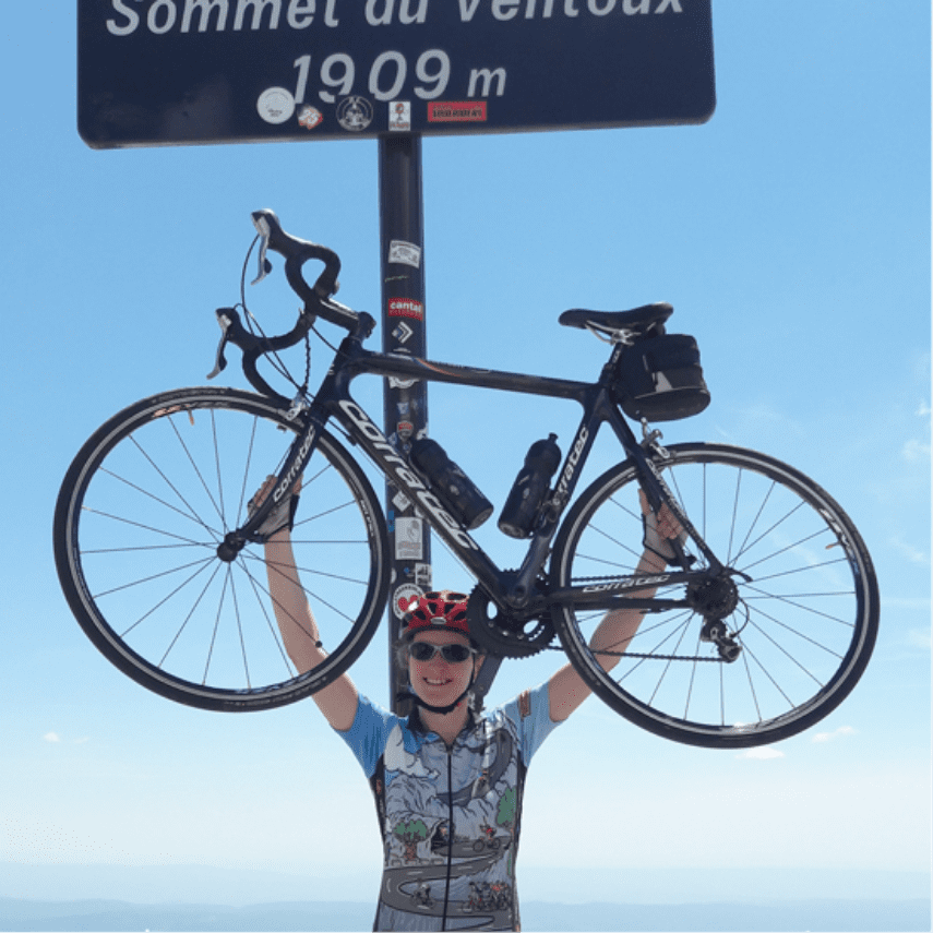 Daniela Pointecker - Jetzt online bei Höllinger bestellen! Daniela Pointecker hält ihr Fahrrad in den blauen Himmel vor einem Schild auf dem "Sommet du Vemoux 1909m" steht.