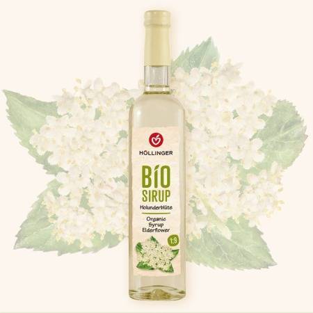 Höllinger Bio Sirup Holunderblüte in Glasflasche vor einem Hintergrund mit Holunderblüten.