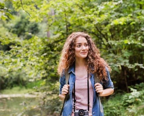 Junge Frau mit Kamera und Rucksack in der Natur