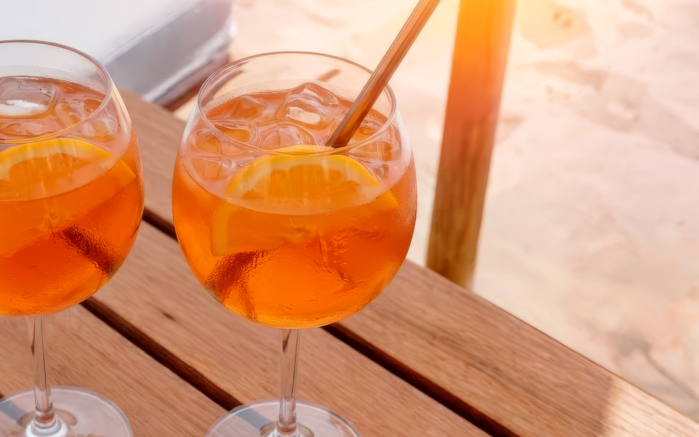 Zwei Gläser Apéro Secco mit Orange auf einem Holztisch in der Sonne