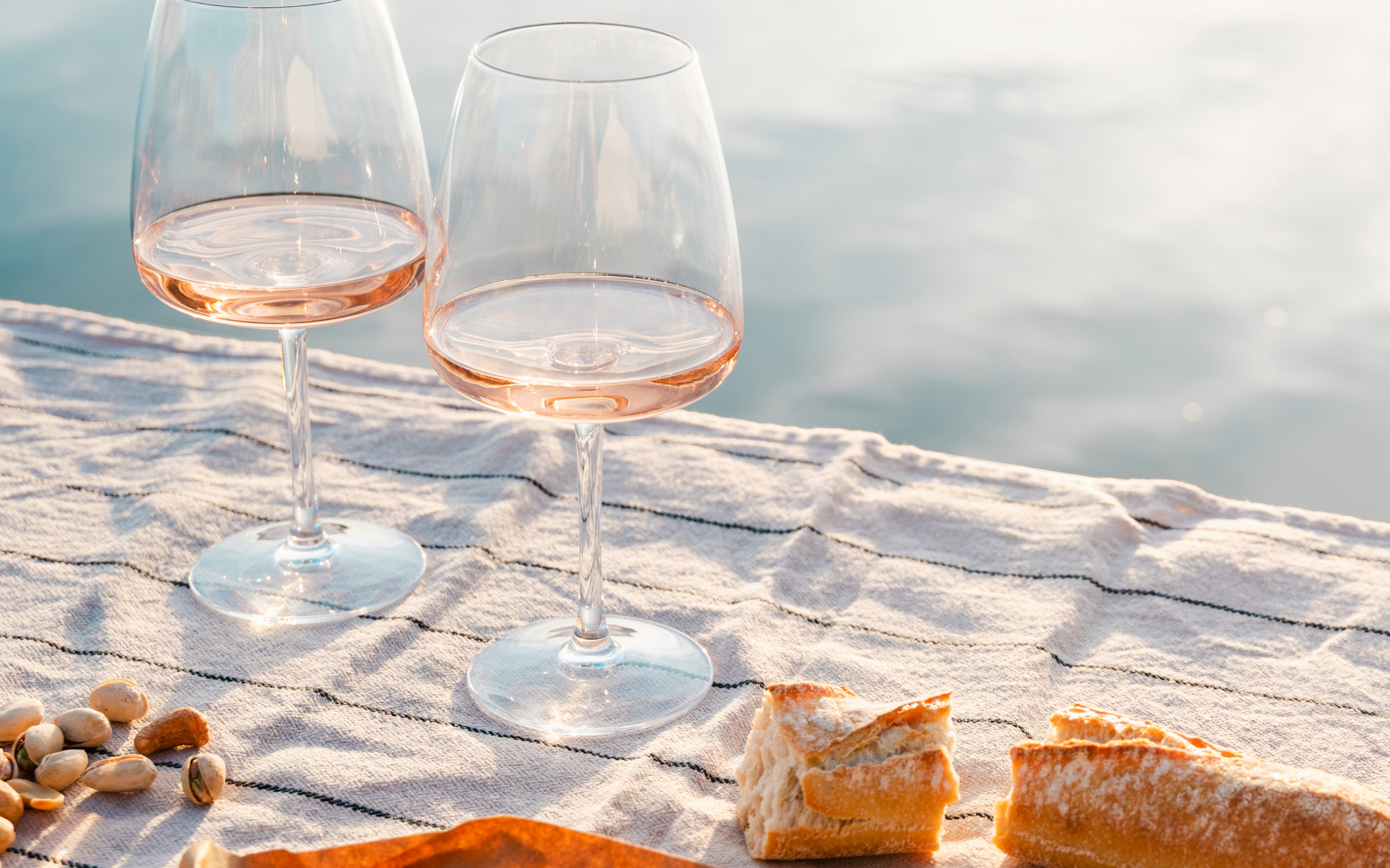 Zwei Gläser Rosé auf einer Picknickdecke mit Baguette am Wasser